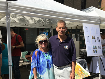 Robert Saasto and wife in front of booth with posters depicting the History of Finns in Harlem and Brooklyn